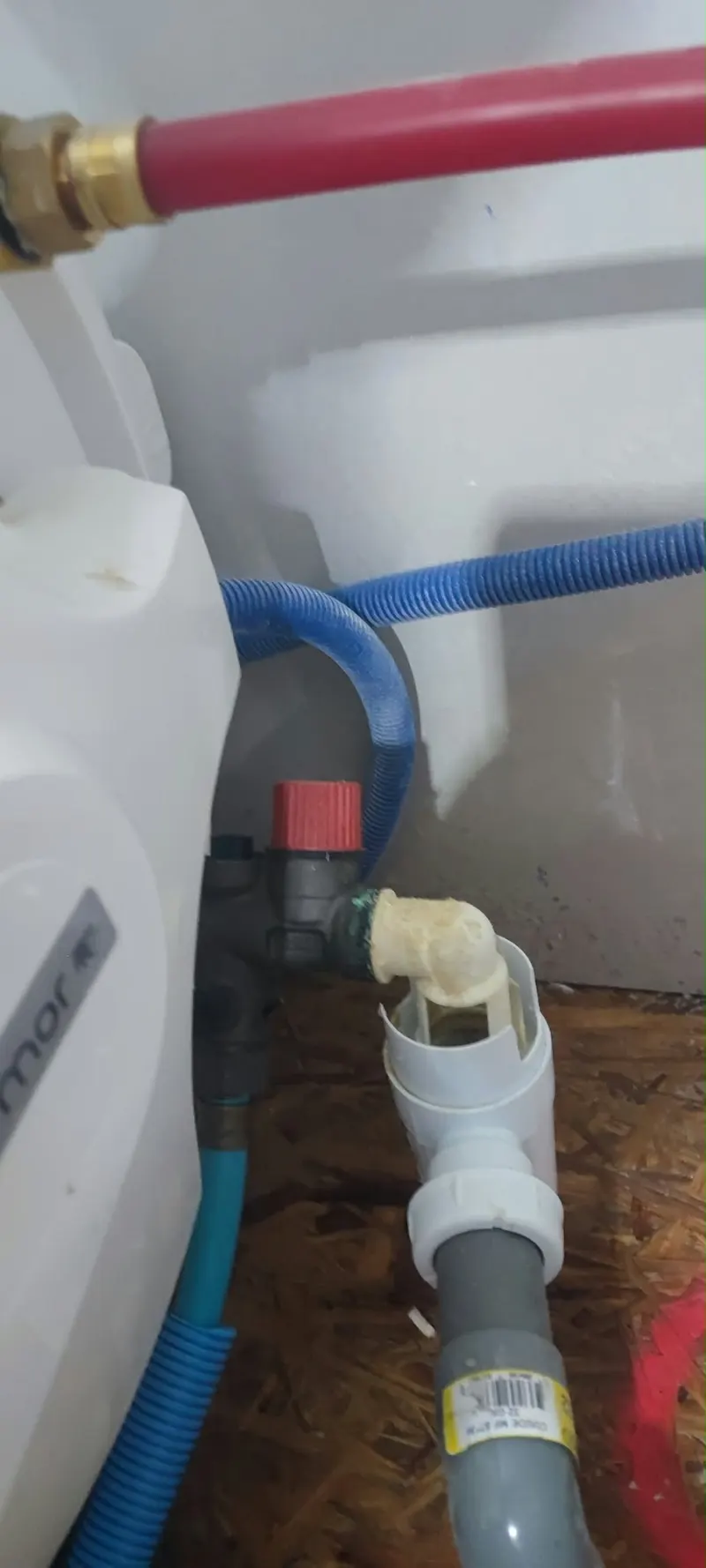 Groupe de sécurité de chauffe-eau avec poignée rouge raccordé à un siphon d'évacuation sous le ballon